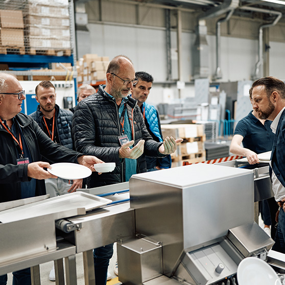 Group of people during a presentation or quality inspection in a HOBART production environment with dishes and machinery