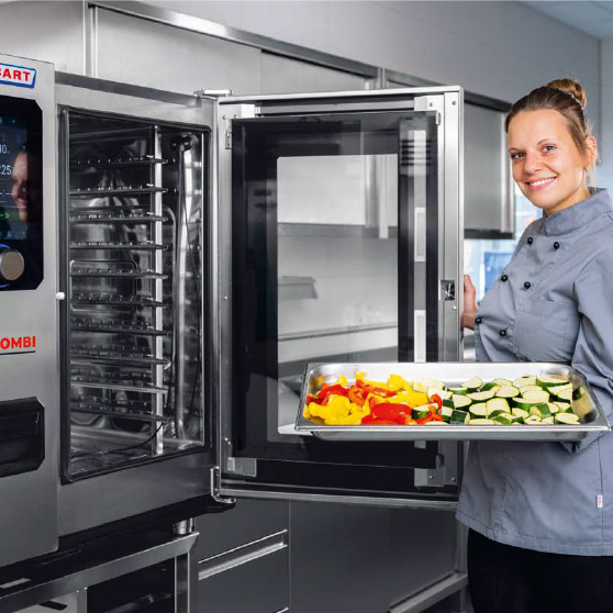 A person in a chef's jacket holds a tray of sliced vegetables such as bell peppers and zucchini in front of an open CHEF'S COMBI oven with multiple racks and a digital control panel.