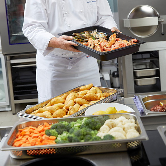 Preparing fresh vegetables, potatoes and seafood in GN containers in a professional kitchen with HOBART GTP cooking technology in the background.