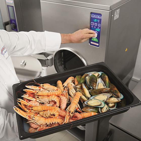 Operating a HOBART dry steam high-speed cooker in a professional kitchen, GN container with prawns and mussels being prepared, modern stainless steel design and digital control panel.